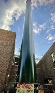 A green cooling tower extends toward the sky. At the base of the tower is a sign that says "DECARBONIZE 95 by 2035."