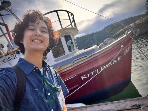 Selfie photo of Isaac next to a boat, the Kittiwake.