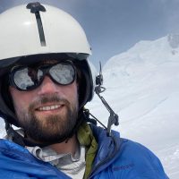 Photo of Liam wearing a helmet and smiling with ice in the background