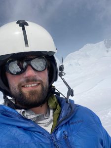 Photo of Liam wearing a helmet and smiling with ice in the background