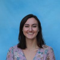 Headshot of Becca smiling in front of a blue blue