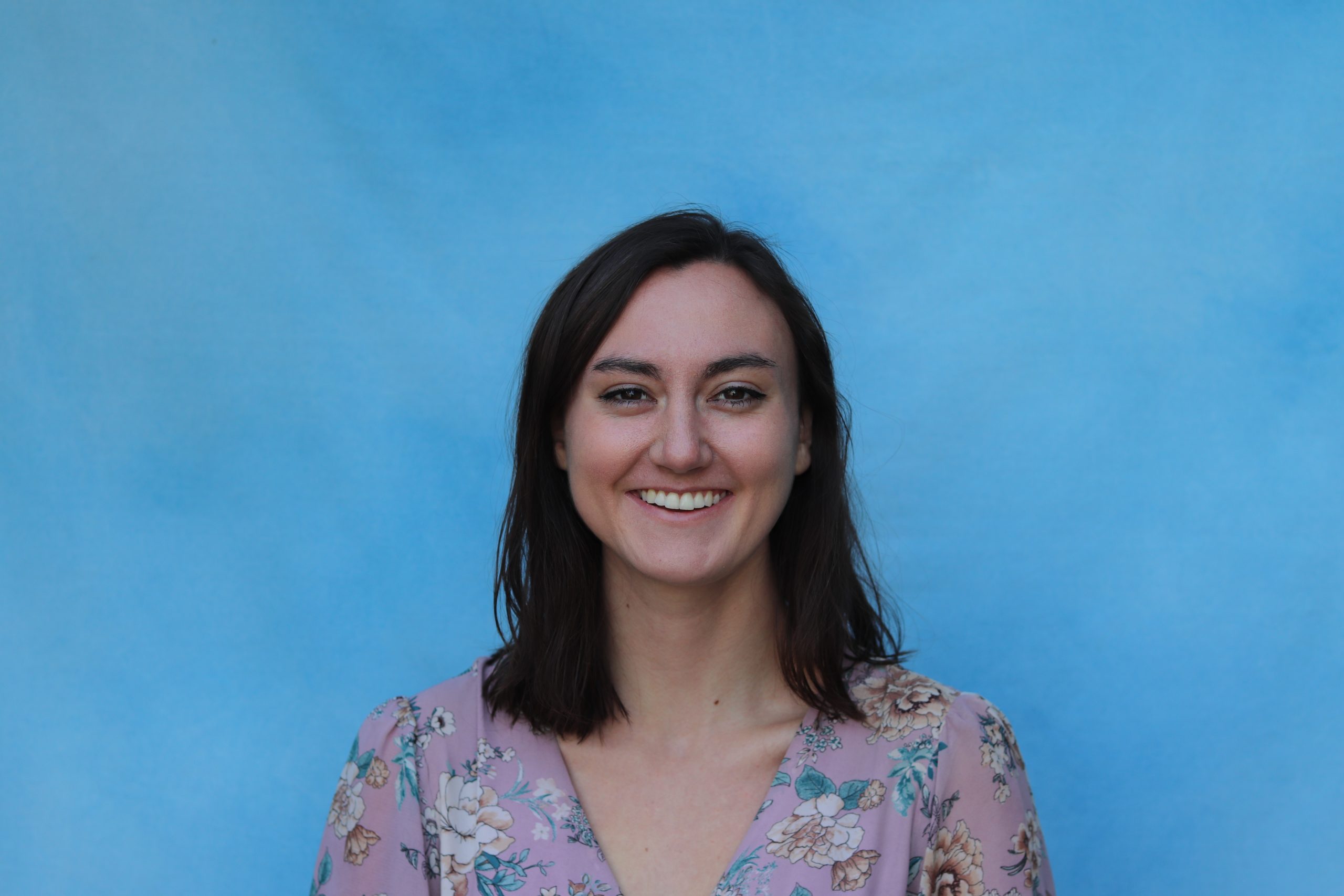 Headshot of Becca smiling in front of a blue blue