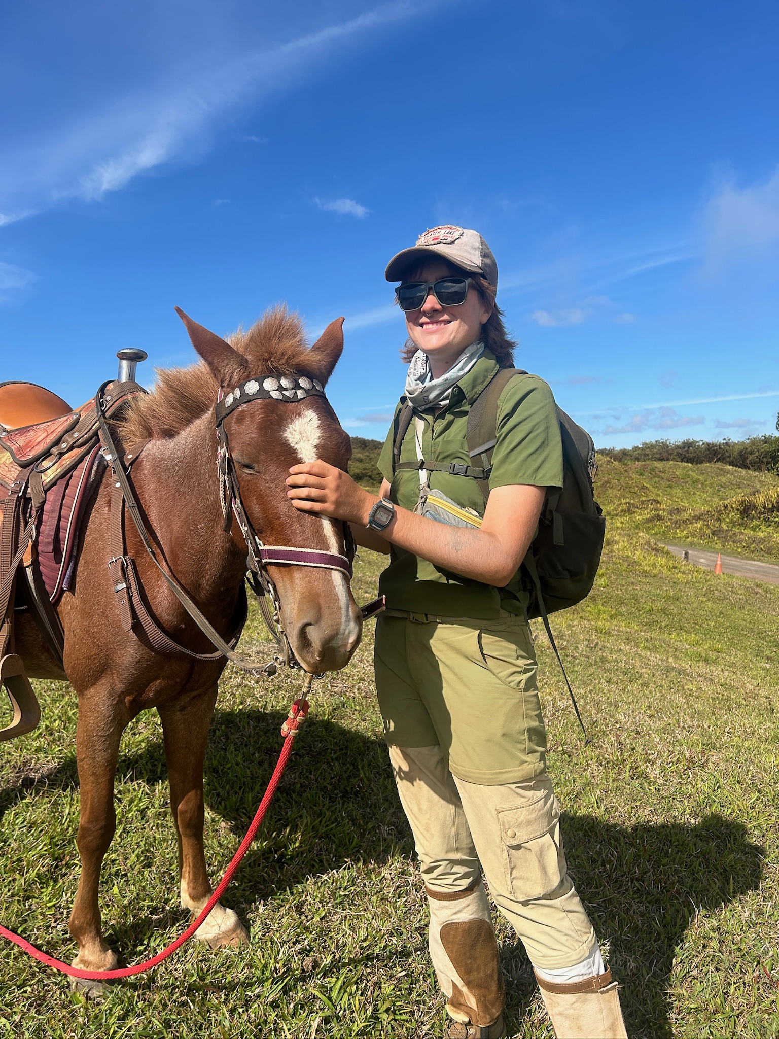 Photo of Ellie outdoors, standing with a horse, and smiling