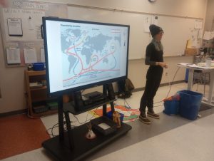 person presenting at front of class room with map model projected on screen