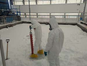 two scientists drilling through snow and ice in hazmat suits