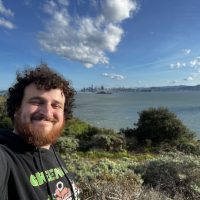 Dylan Arius Harootunian selfie smiling in front of large body of water