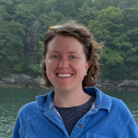 Heili Lowman Headshot smiling in front of a lake surrounded by vegetation