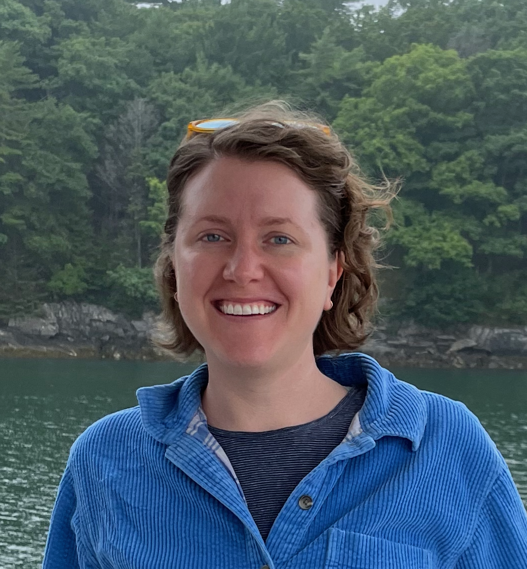 Heili Lowman Headshot smiling in front of a lake surrounded by vegetation